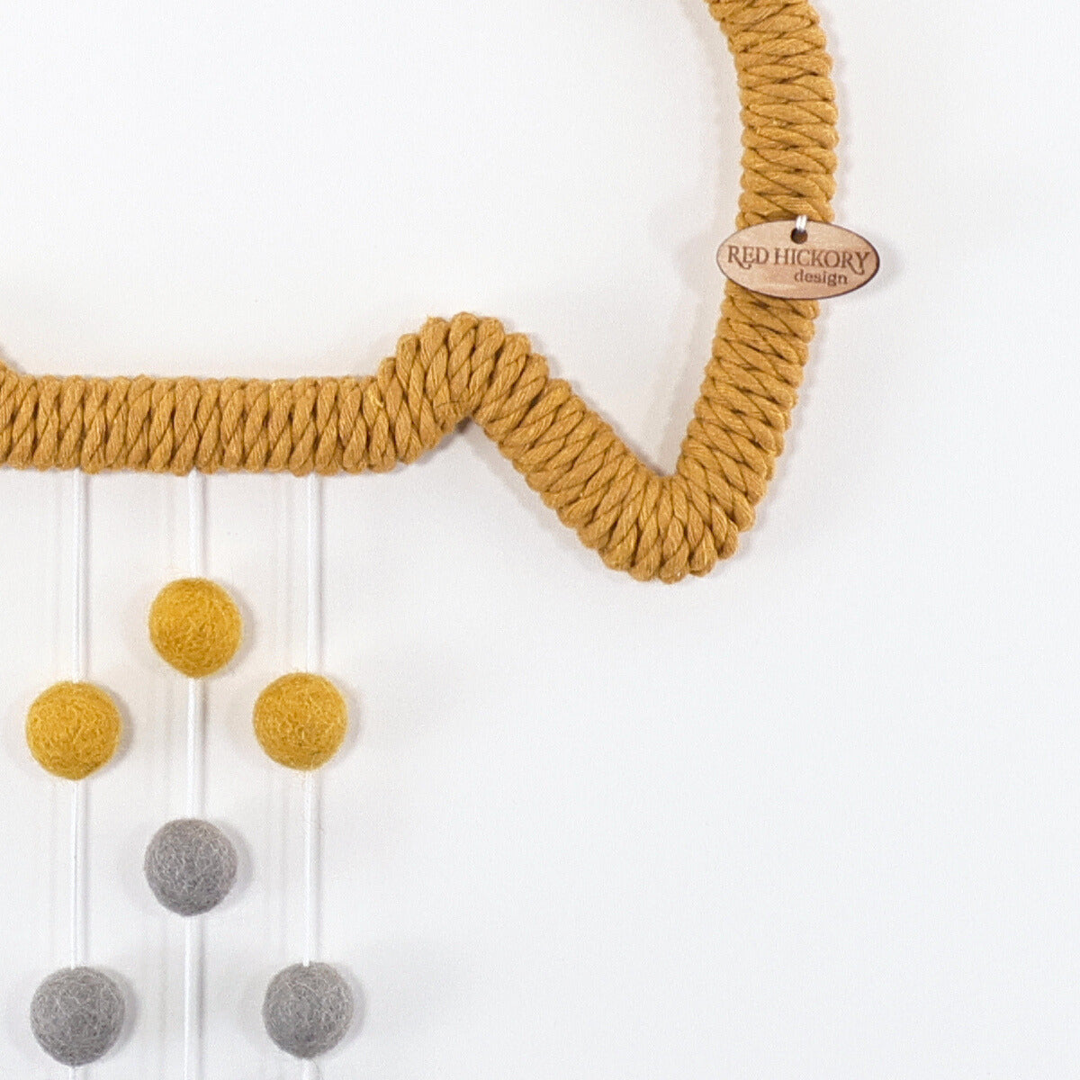 Yellow rocket shape wooden frame is wrapped with mustard yellow cotton yarn. Wool felt gray star hanging from the nozzle. Trails of wool felt pom-poms in blue, yellow, gray hanging from the bottom.